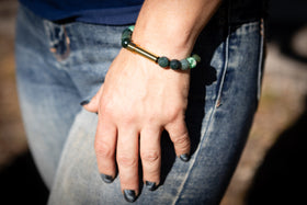 Hand wearing a cremation bracelet with moss agate and flower beads, resting on a blurred background