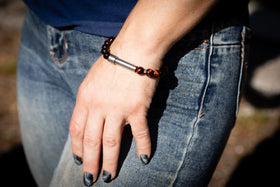 Hand wearing a cremation bracelet with beads, wearing blue jeans outdoors.
