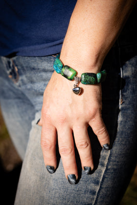 Close-up of a hand wearing a green beaded cremation bracelet with a small charm.