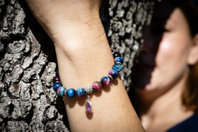 Multicolored beaded bracelet on a wrist with a blurred background with an amethyst drop holding cremation ash