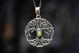 Silver tree of life pendant with a green gemstone and cremation ash on a dark background