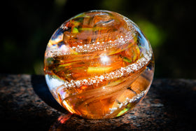 Clear glass cremation orb with internal patterns on a dark surface