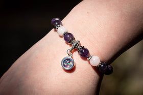 Photo depicts the amethyst and rose quartz healing bracelet on a model's wrist. The dainty circle charm, made with turquoise and magenta opal, faces towards the viewer. Rose quartz bracelet, rose quartz jewelry, amethyst bracelet, amethyst jewelry, natural stone jewelry, remembrance jewelry, jewelry for cremation ash, bracelet for ash