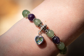 Photograph depicts the aventurine and amethyst bracelet on a wrist. The dainty heart charm, containing green and light blue opal, is attached and faces towards the viewer.  Amethyst bracelet, aventurine bracelet, natural stone bracelet, remembrance jewelry, bracelet for cremation ash