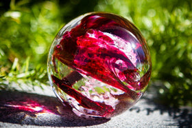 ruby red orb with cremation ash sitting in sunlight in front of bush
