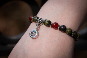 Photograph depicts the Dragon Agate and Red Agate bracelet on a wrist. The dainty circle charm, containing black and white opal, is attached and faces towards the viewer. Dragon Agate bracelet, Red Agate bracelet, natural stone bracelet, remembrance jewelry, bracelet for cremation ash
