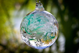 teal and white glimmer orb hanging outside in sun with cremation ash