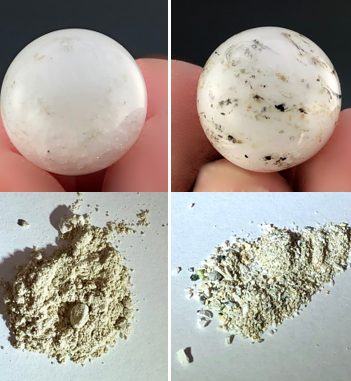 Two white cremation spheres with gold and speckled ash powder beside them on a blue-gray surface