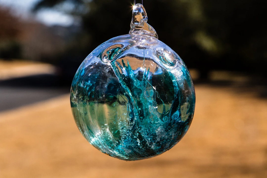 Teal glass memorial ornament hanging outdoors, catching sunlight with a blurred yard background
