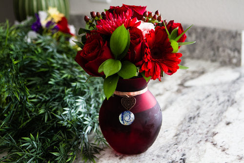 Vase memorial with red roses in a dark burgundy vase on a marble countertop.