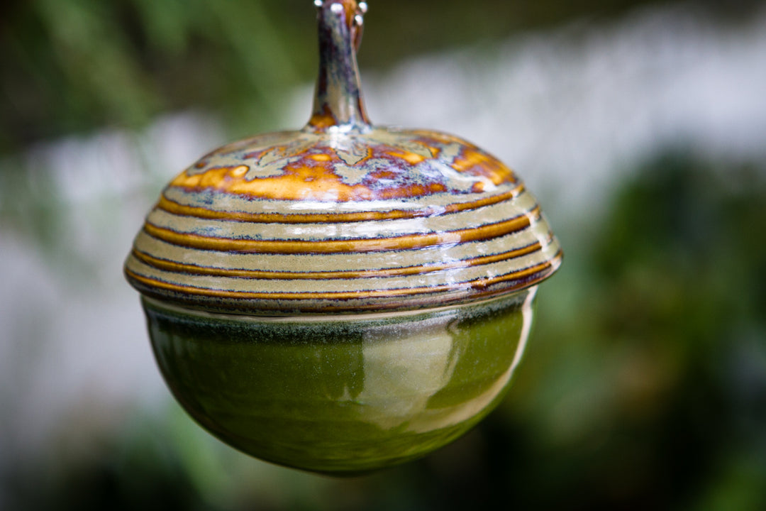 Garden ceramic acorn keepsake urn with green bottom and striped lid.