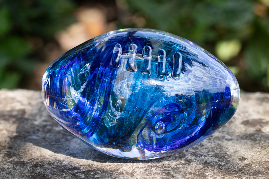 blue glass football with cremation ash sitting on stone bench