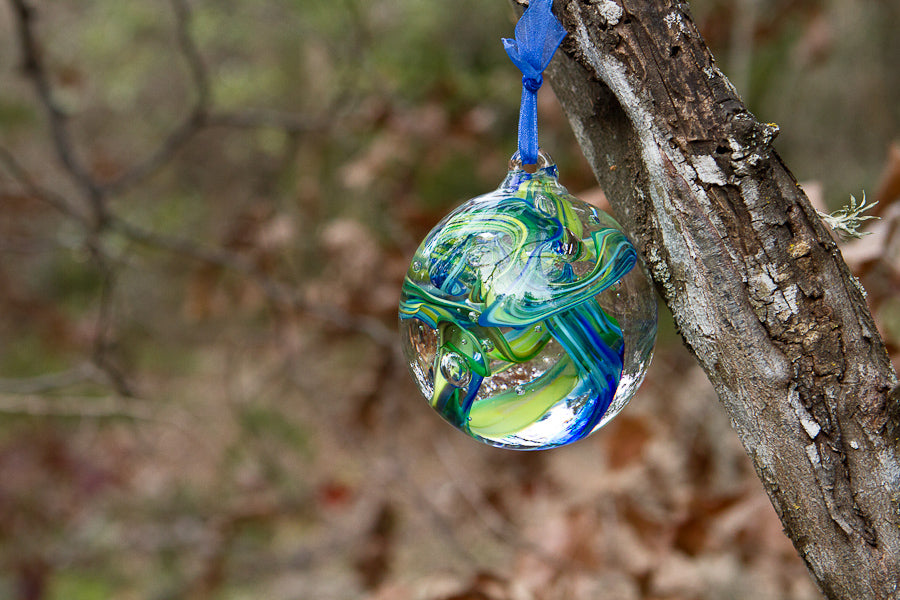 Dog memorial glass ornament with blue and green swirls hanging from a tree branch