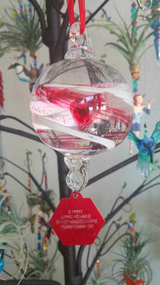 Memorial cremation glass ornament with a red heart inside and white swirl ribbons, hanging from a red ribbon.