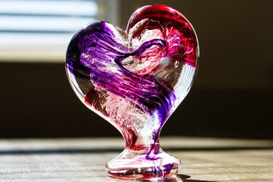 Standing glass heart sculpture with purple and pink swirls of cremation ash.