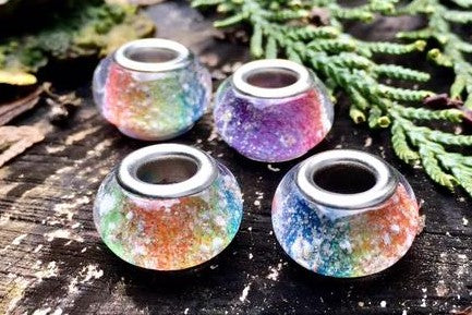 Four multicolored iridescent glass beads with metal cores on a weathered wooden surface with greenery