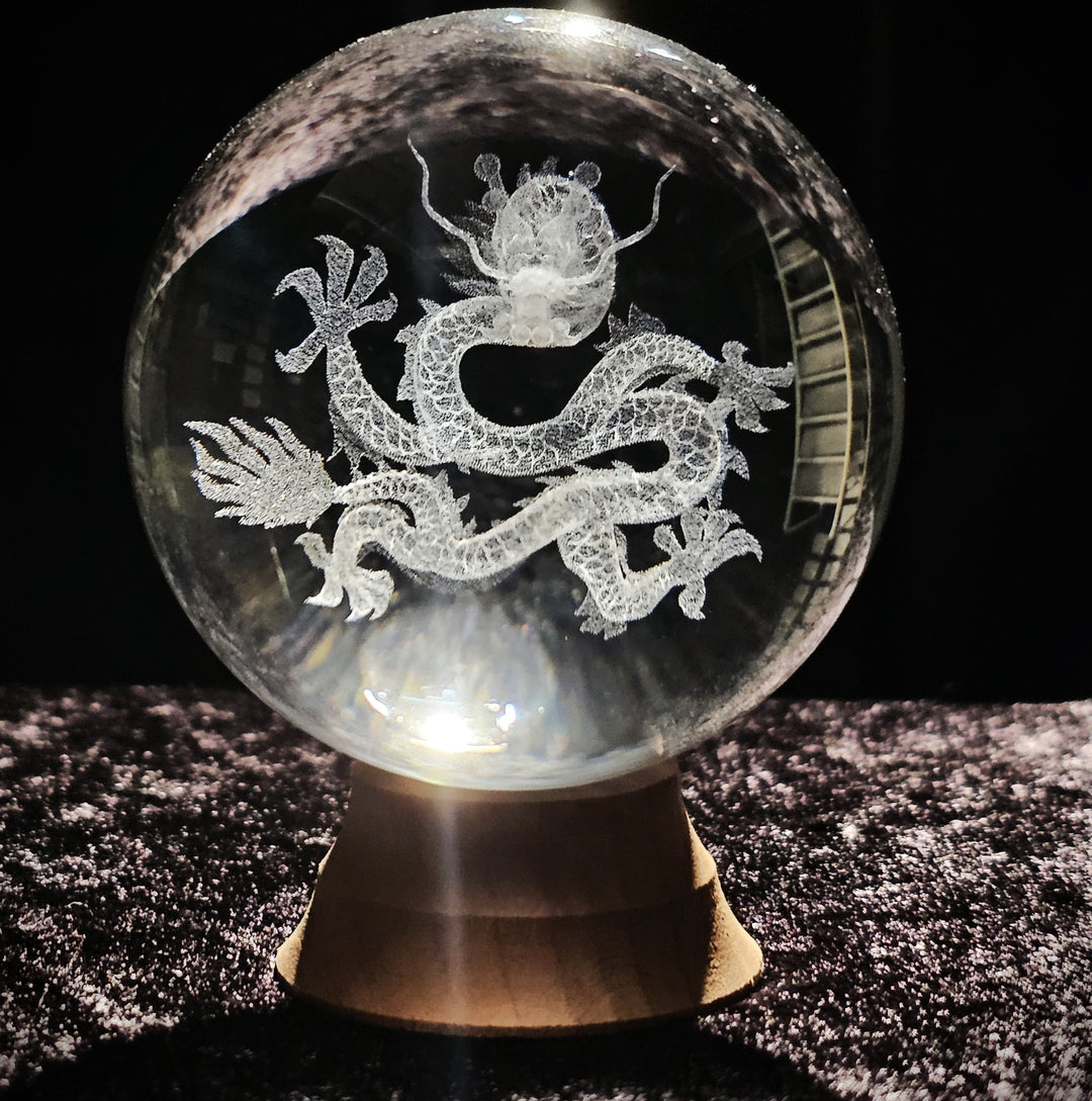 Crystal sphere showing an etched dragon perched on rocks with a moon in the background on a wood stand