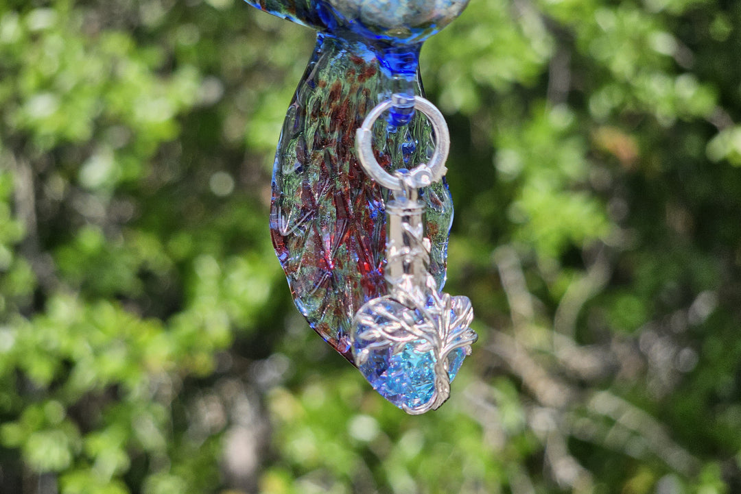 Close up of blue glass hummingbird pendant with a beaded strand and crystal leaf charm.