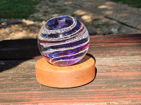 Glass orb with purple and white stripes on a wooden urn outdoors