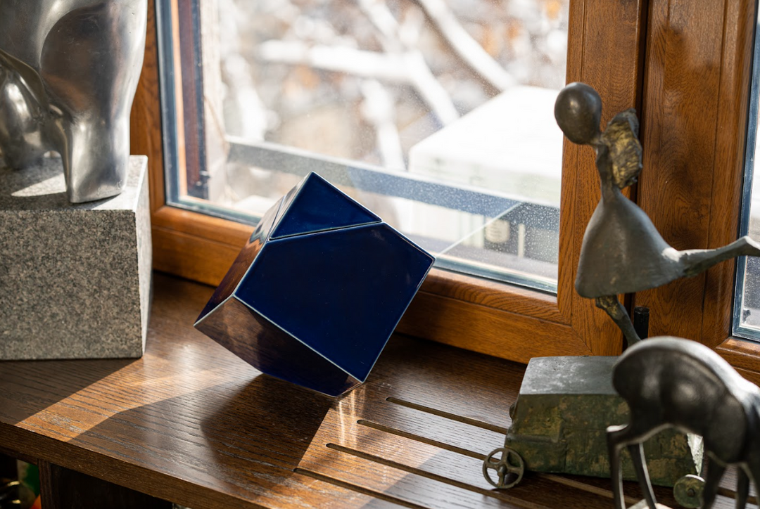 Blue glossy abstract ceramic urn balanced on its edge on a wooden table by a window