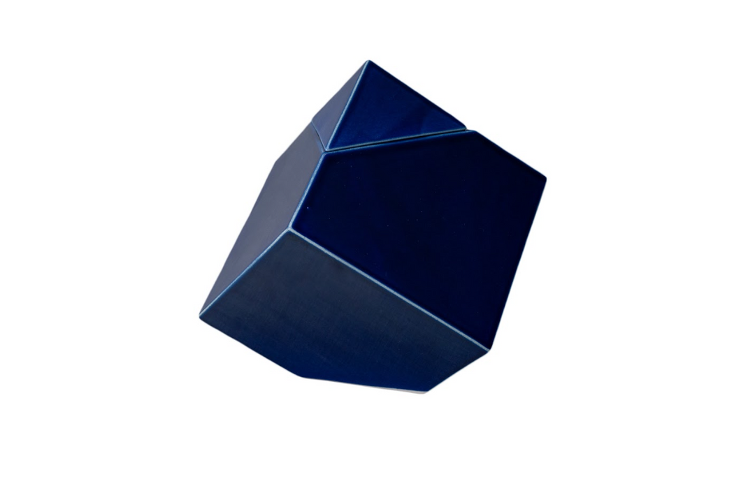 Deep blue abstract ceramic urn with angular facets resting on its edge, designed for candle remembrance.