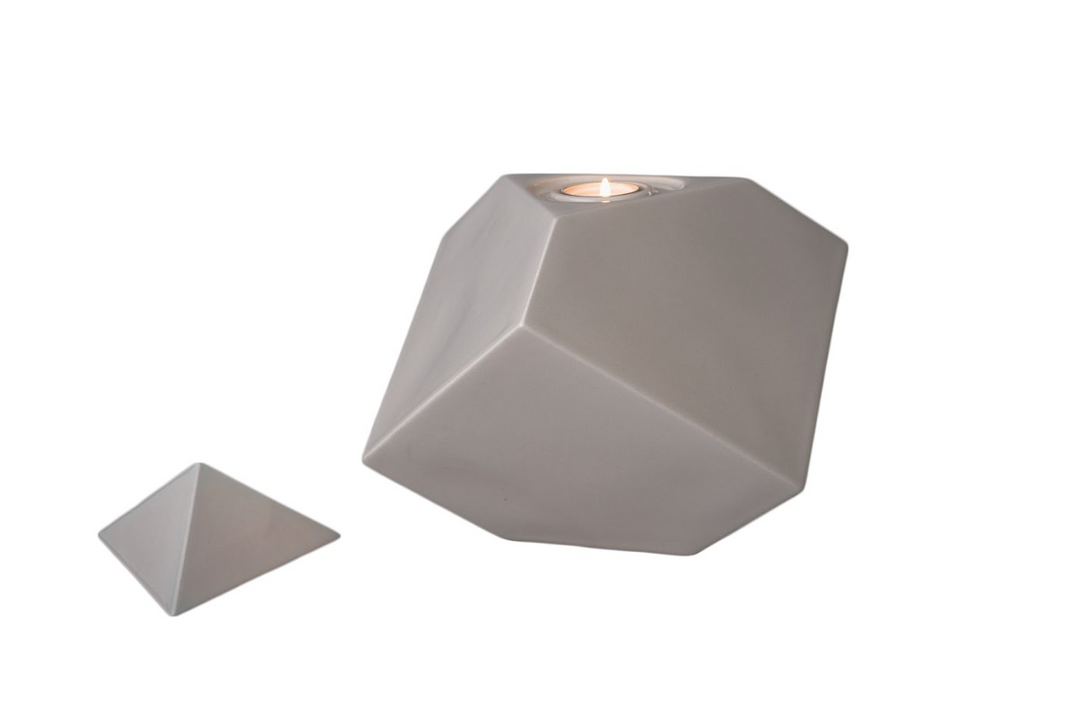 Faceted gray ceramic urn with a candle holder on top and a separate lid resting beside.