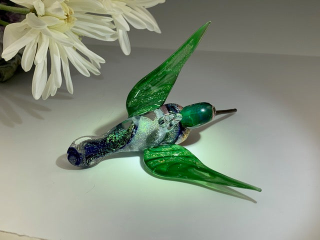 Side view of Anna's dichroic hummingbird with emerald green wings and glittery body on a white surface.