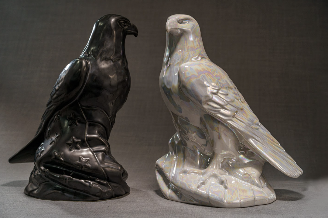 Pair of Aquilae ceramic memorial urns shaped as eagles in black and iridescent white finishes.