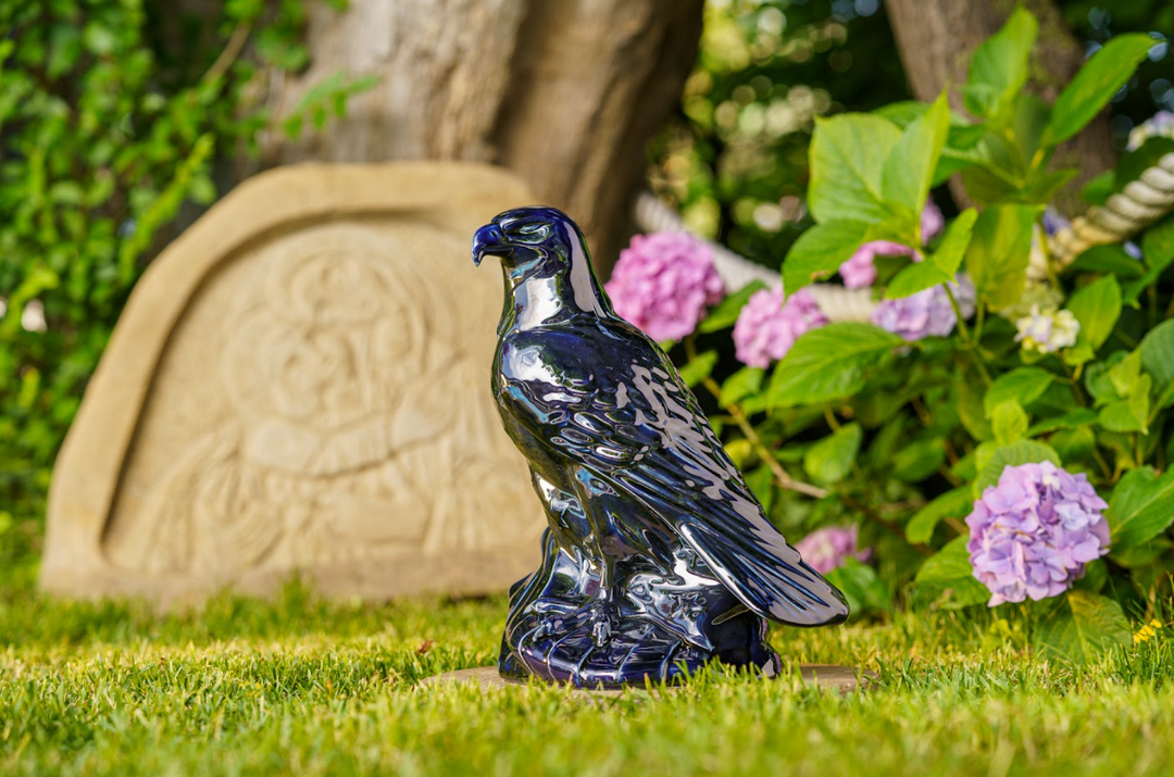 Glazed blue ceramic eagle statue on a rock base in a garden setting