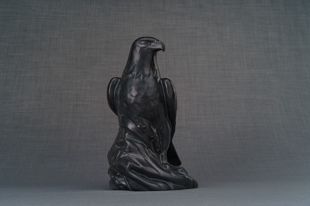 Dark gray ceramic urn showing a perched eagle on a sculpted base with draped details