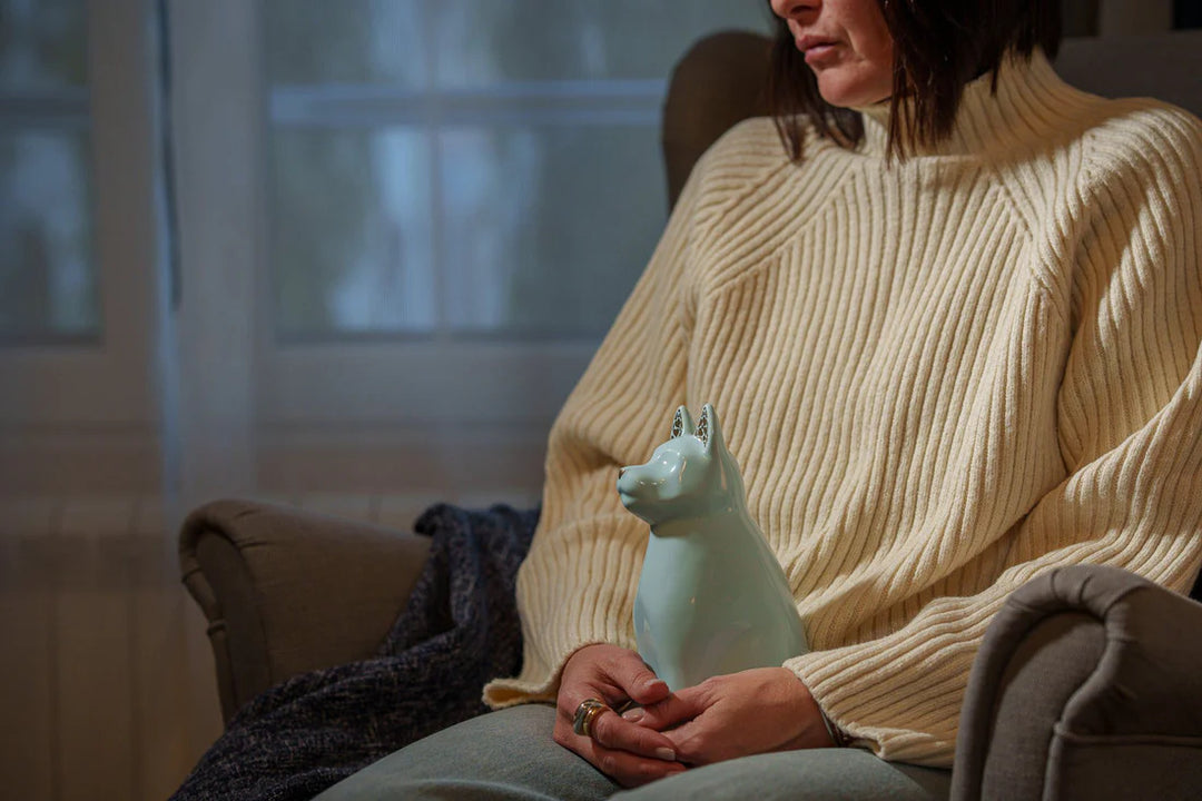 Soft blue Barkley dog ceramic urn being held in a person's lap.