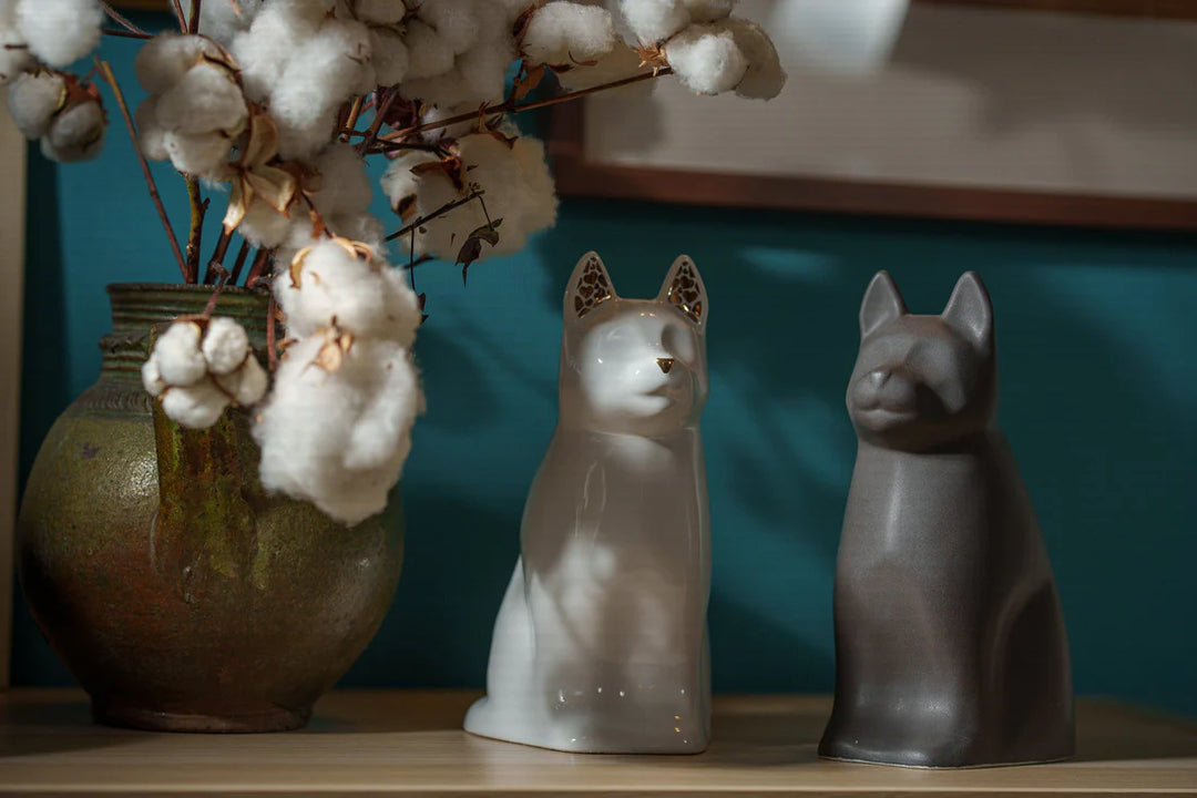 Two Barkley Dog Ceramic Urns, a white one with gold ear lattice and a dark gray companion beside it