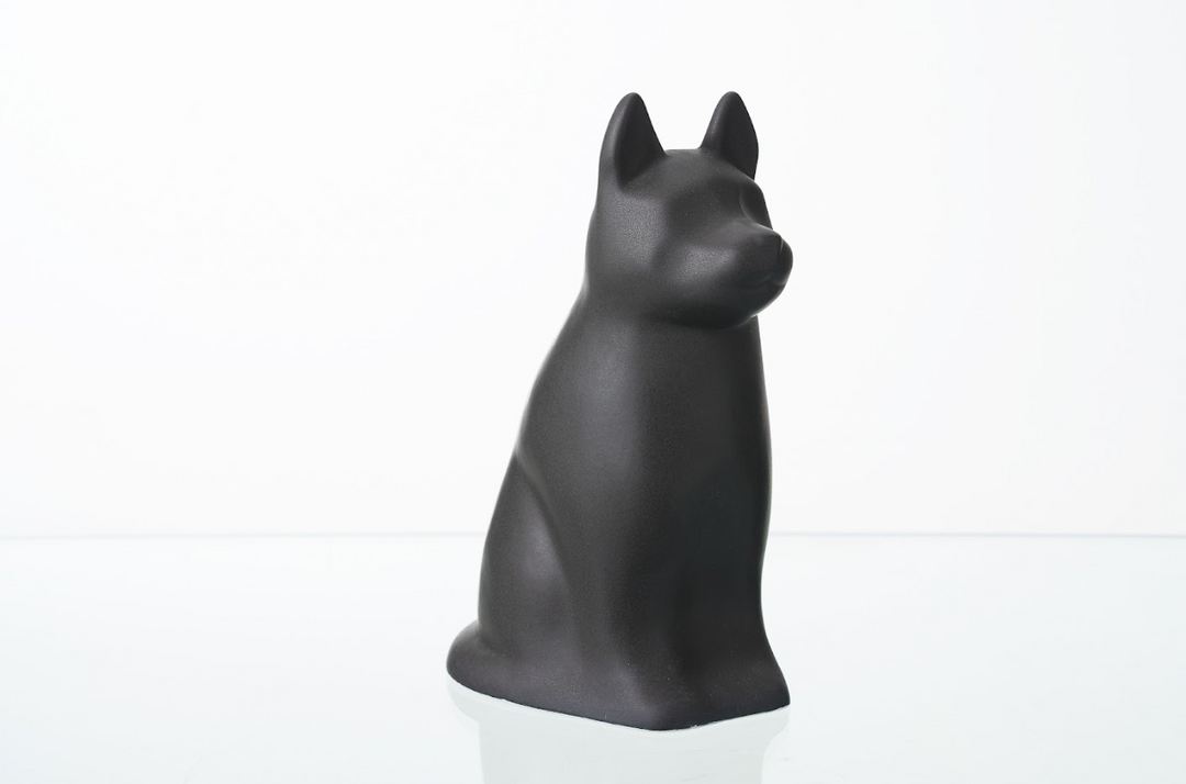 Matte black Barkley dog ceramic urn in a seated pose on a white surface.