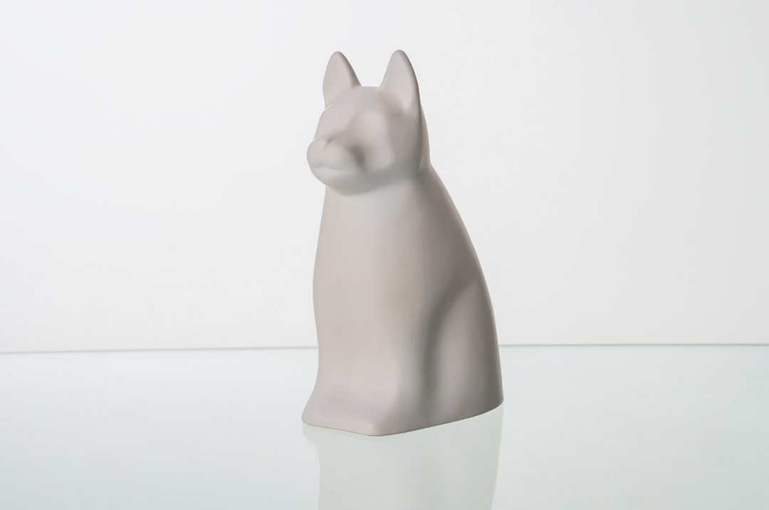 Pale gray dog shaped ceramic urn on a glass surface