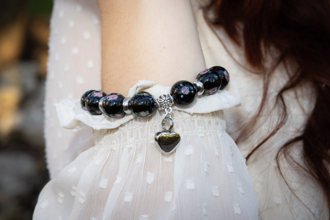 Black glass flower bracelet with silver spacers worn on the wrist and a dangling heart keepsake charm