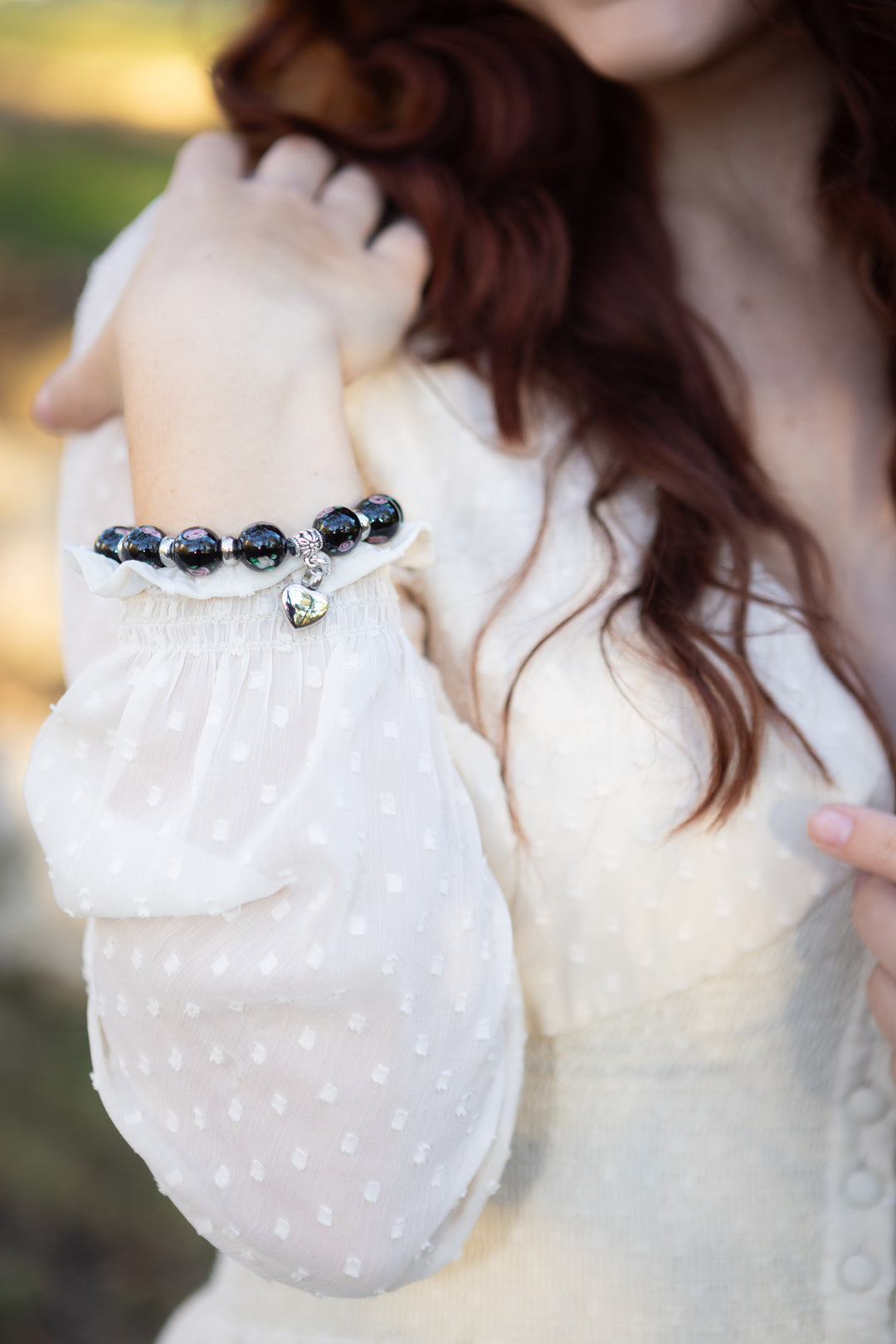 Close up of black glass floral bracelet with a heart keepsake pendant on the wrist