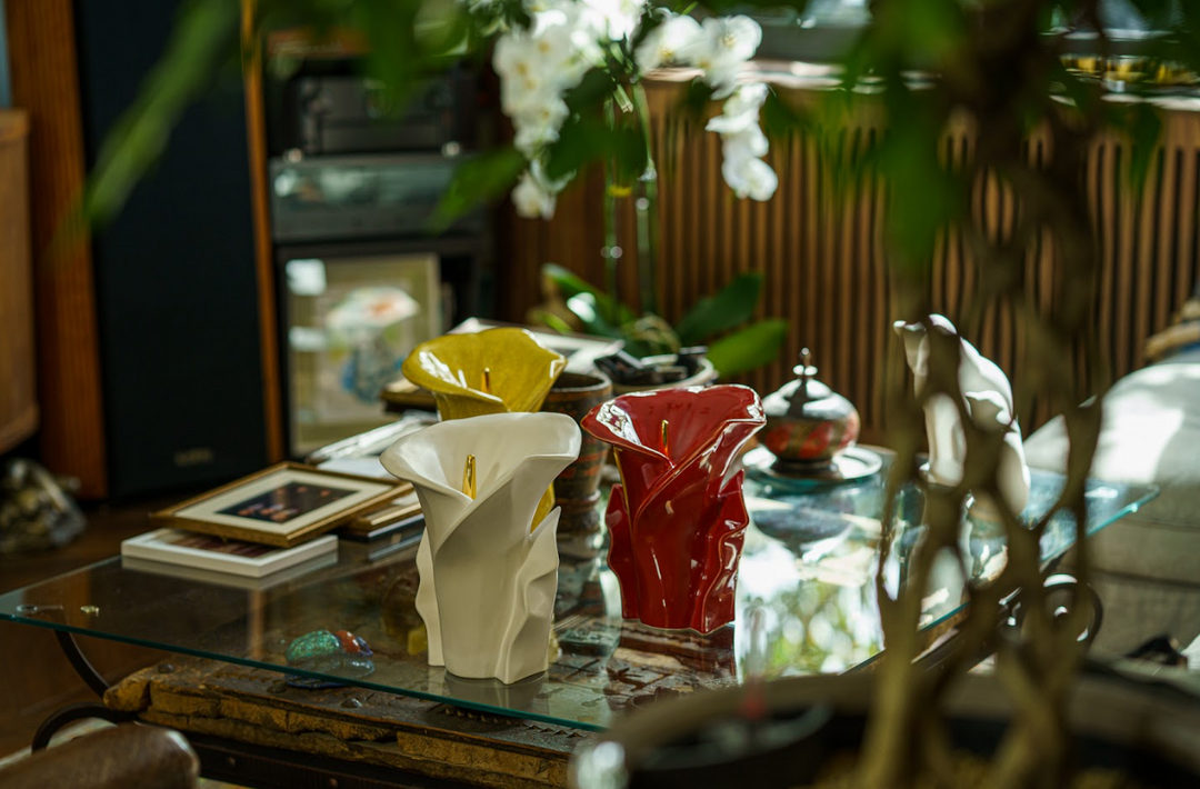 Three ceramic calla lily vessels in white yellow and red displayed on a glass coffee table in a cozy living room setting
