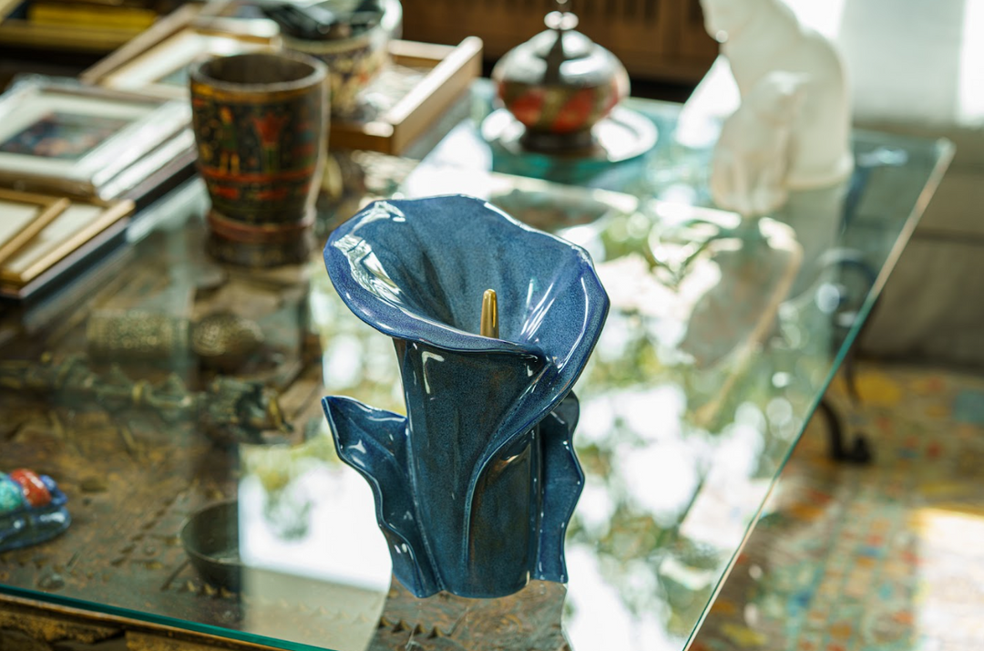 Blue glazed Calla Lily ceramic urn with a gold accent, shown on a glass coffee table among decorative items.