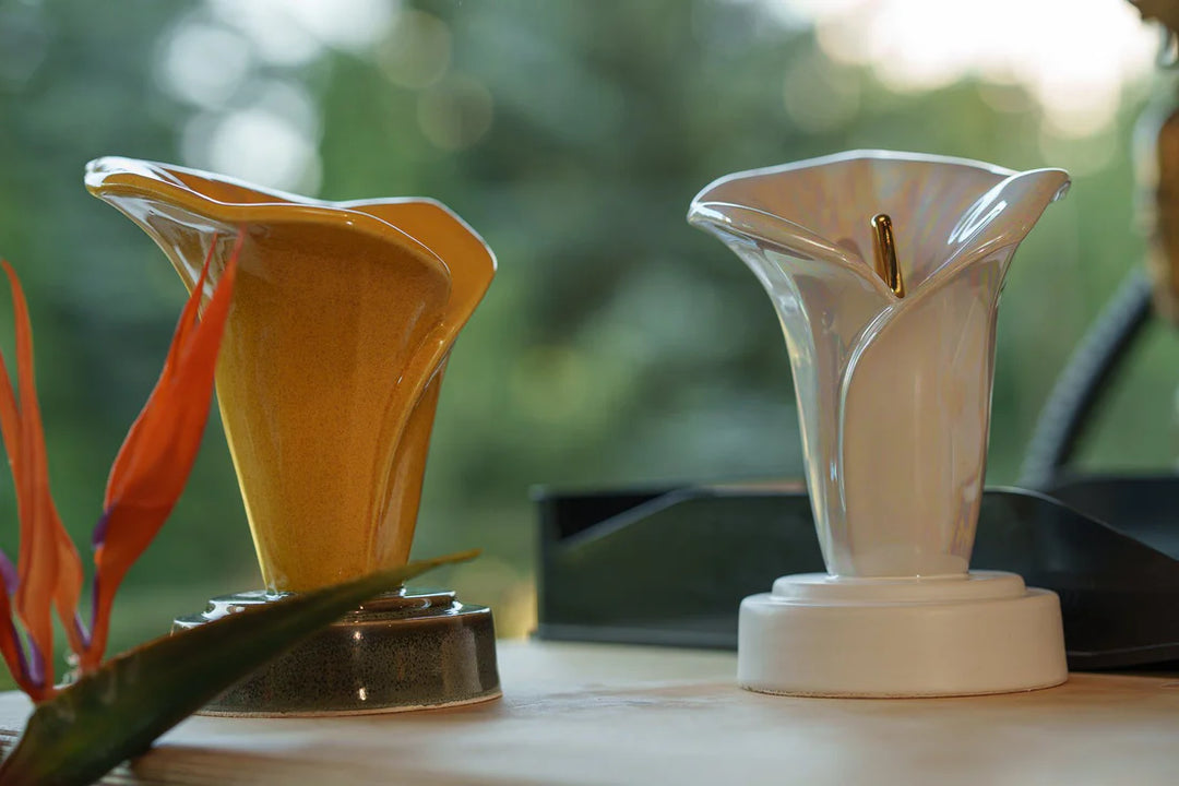 Pair of glass calla lily keepsake sculptures in orange and white with gold centers on round bases.