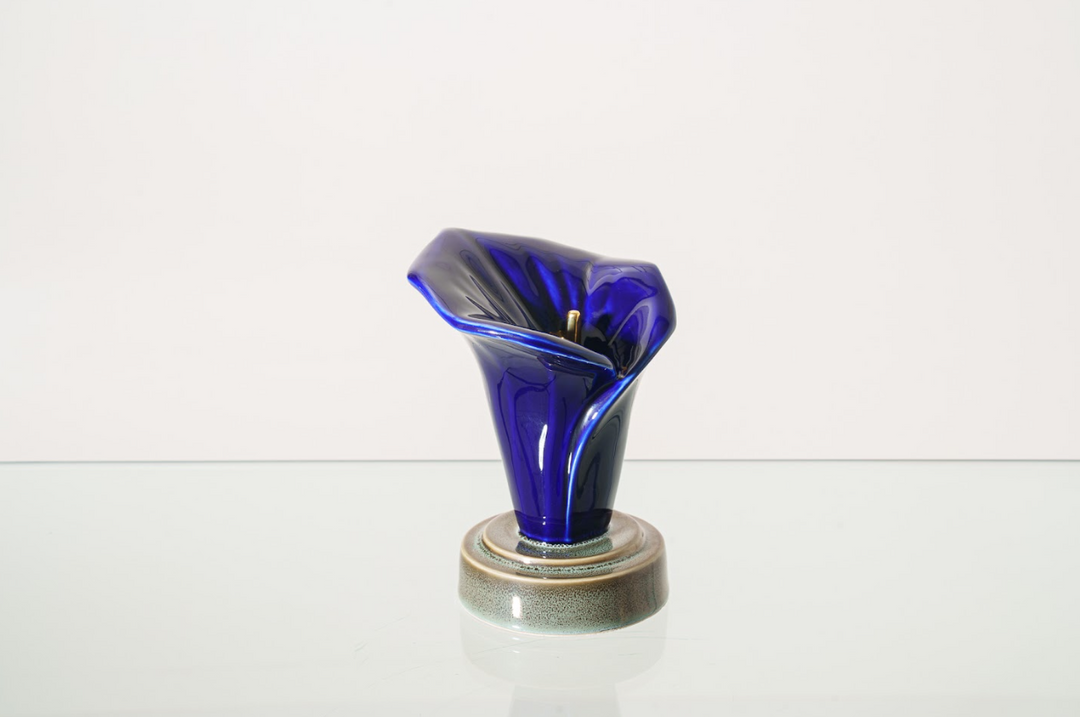 Deep blue glass calla lily sculpture on a textured round ceramic base.