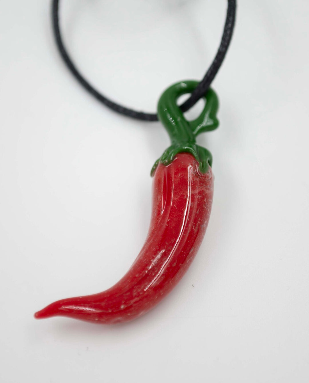 Red glass chili pepper pendant with green stem on a black cord infused with cremation ashes.