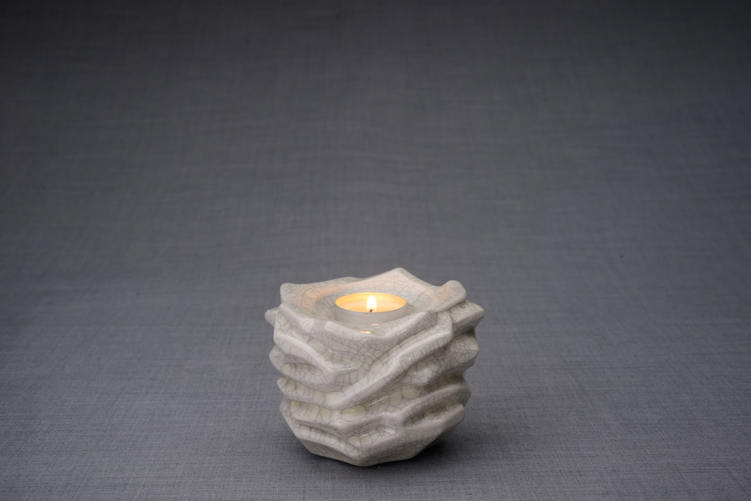 Close up of crackled white ceramic candle holder with a lit tealight on a gray backdrop.