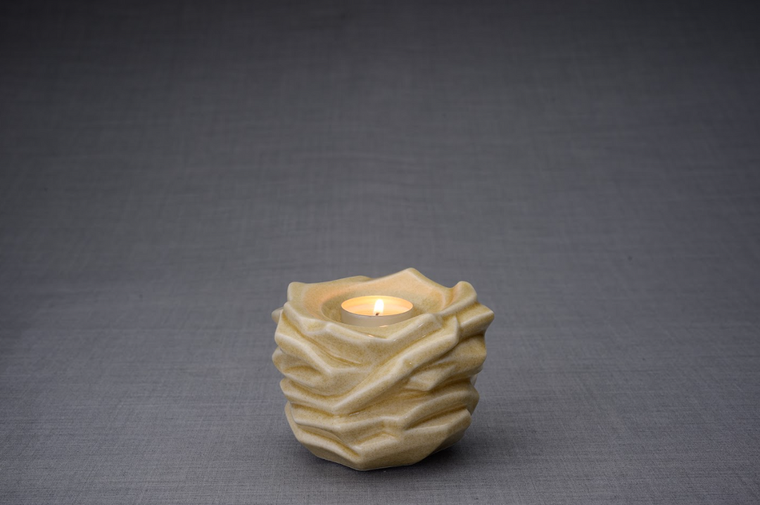 Beige Christ Ceramic Urn with a lit tealight in a wave textured top opening.
