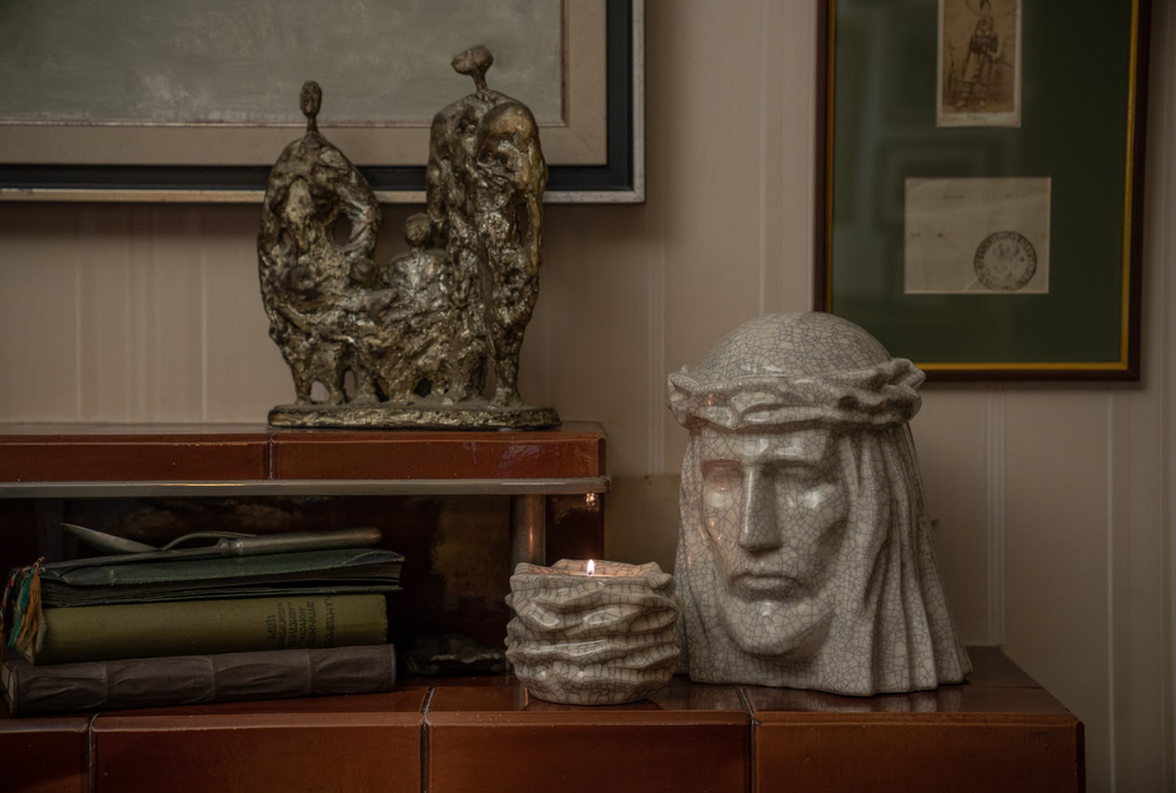 Crackled white ceramic candle holder with a lit tealight beside a Christ bust on a wooden surface.