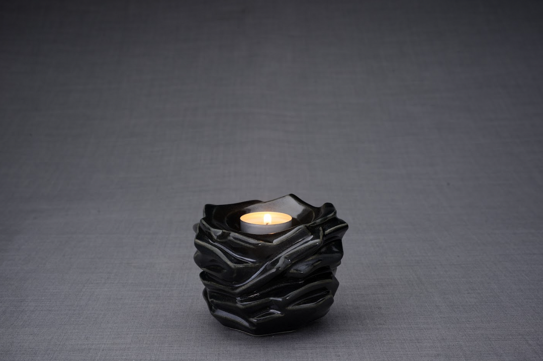 Black gloss Christ Ceramic Urn with a lit tealight resting in the sculpted wavy top opening.