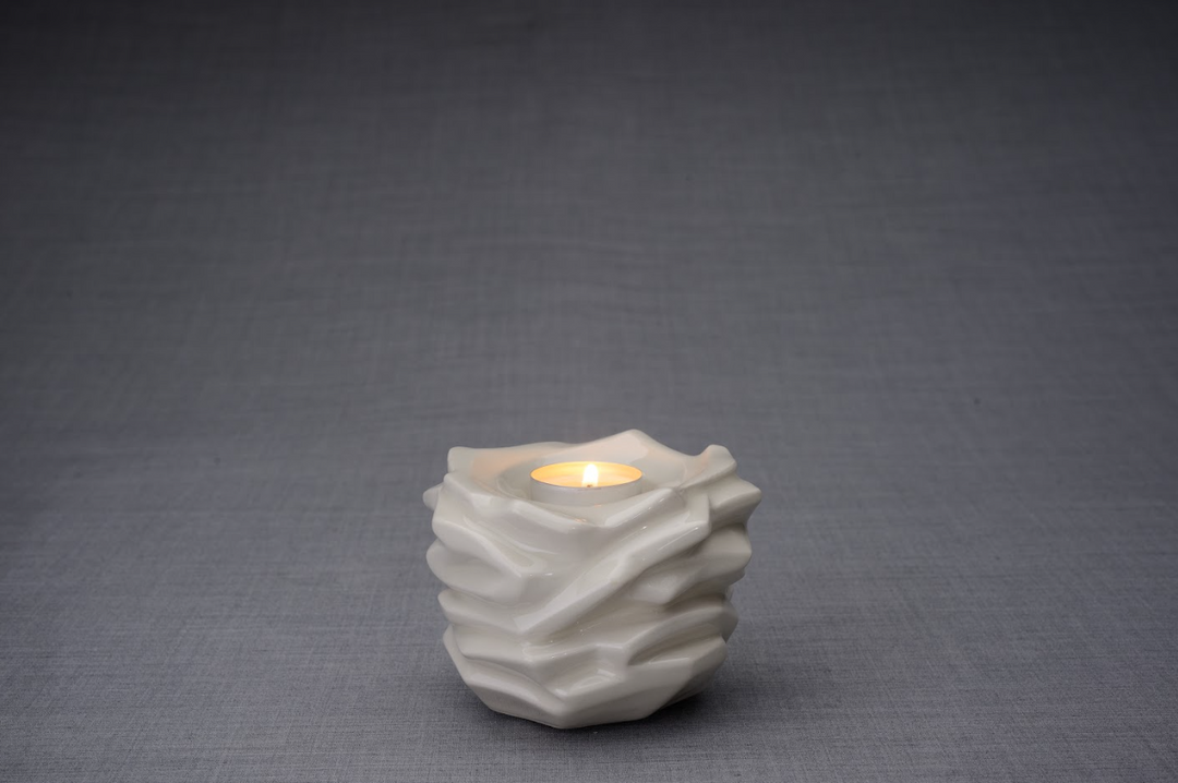 White Christ ceramic urn with flowing folded surfaces and a lit tealight