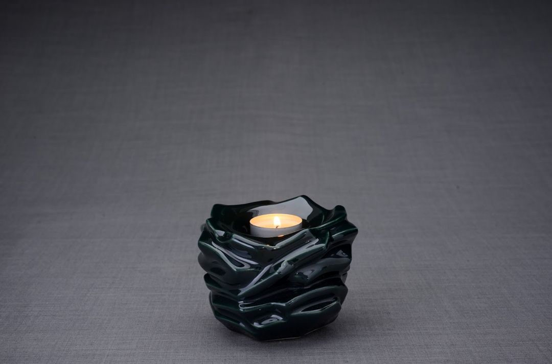 Dark green sculpted ceramic urn with waves and a lit tealight at the opening