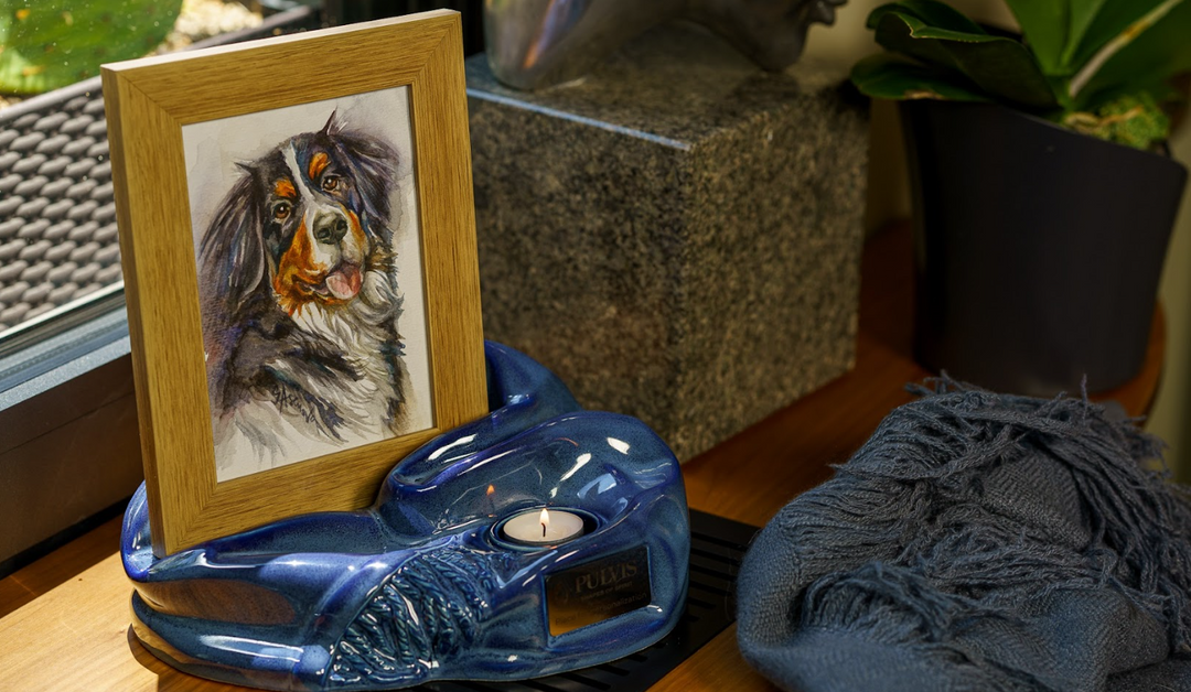 Dog portrait in a wooden frame leaning on a glossy blue ceramic urn with a small candle.