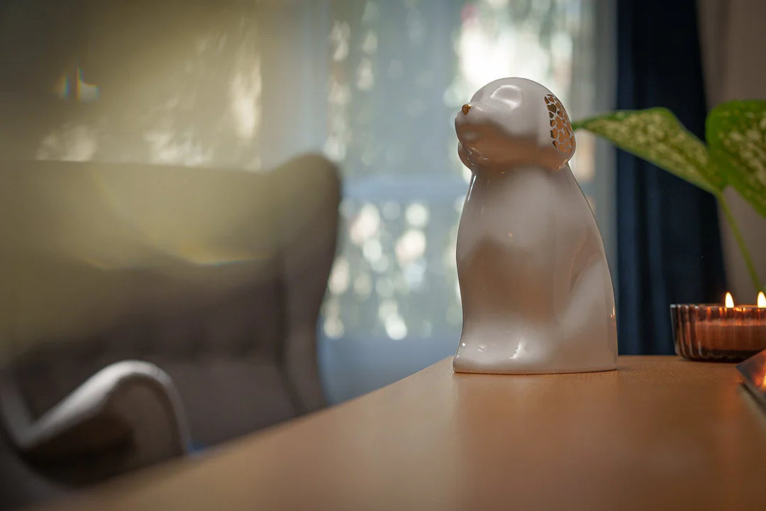 Cuddle Dog ceramic urn shaped like a sitting dog with gold lattice ears on a wooden table beside a lit candle.