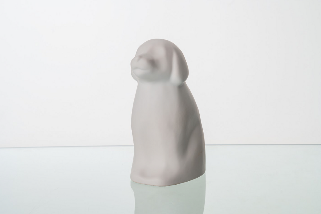 Pink dog shaped ceramic urn with gold lattice ear detail against a white backdrop